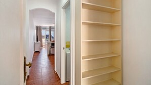 A hallway with a white door, a white wall, and a white closet with multiple shelves.