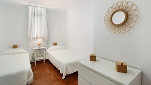 A bedroom with two beds, a bedside table with a lamp, a dresser, a mirror, and a curtain.