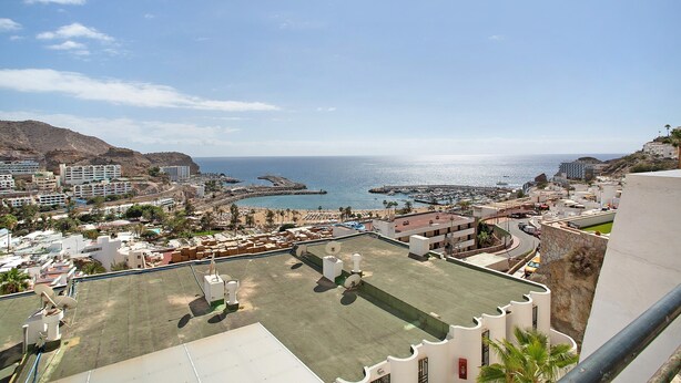 A rooftop terrace with a view of the sea, buildings, and a mountainous backdrop.