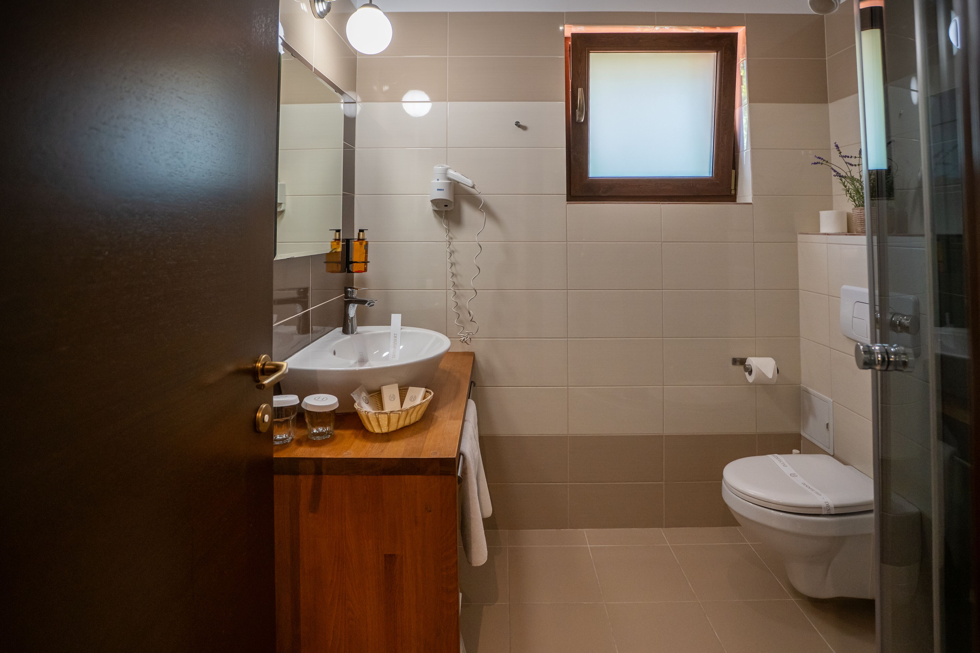 Un baño con tocador de madera, lavamanos blanco, espejo, toallero, inodoro y cabina de ducha de vidrio.