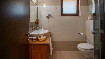 Un baño con tocador de madera, lavamanos blanco, espejo, toallero, inodoro y cabina de ducha de vidrio.