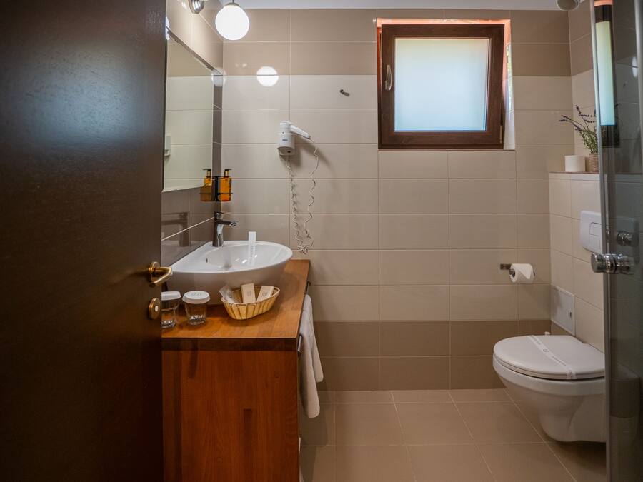 Un baño con tocador de madera, lavamanos blanco, espejo, toallero, inodoro y cabina de ducha de vidrio.
