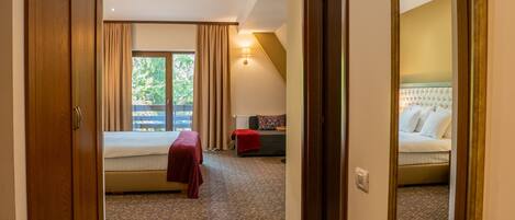 A hotel hallway with a patterned carpet, a bed with a red blanket, and a large mirror on the wall.