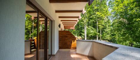 Un pasillo exterior cubierto con una escalera de madera que conduce a un nivel superior, rodeado de follaje.