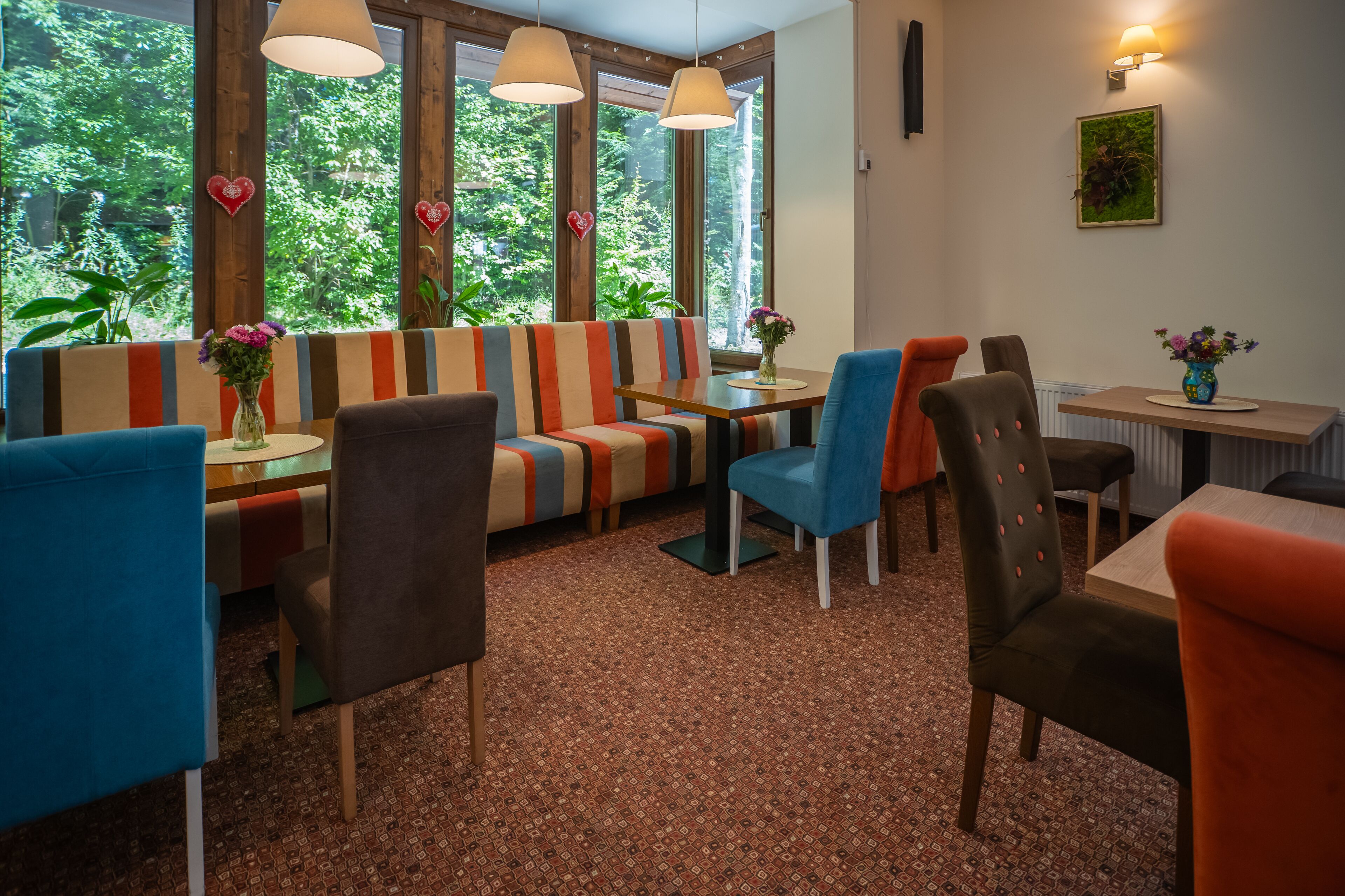 A dining area with striped seating, a wooden table, and a view of greenery through large windows.