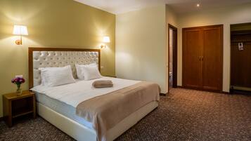 A hotel room with a large bed, two bedside lamps, a wooden wardrobe, and a carpeted floor.