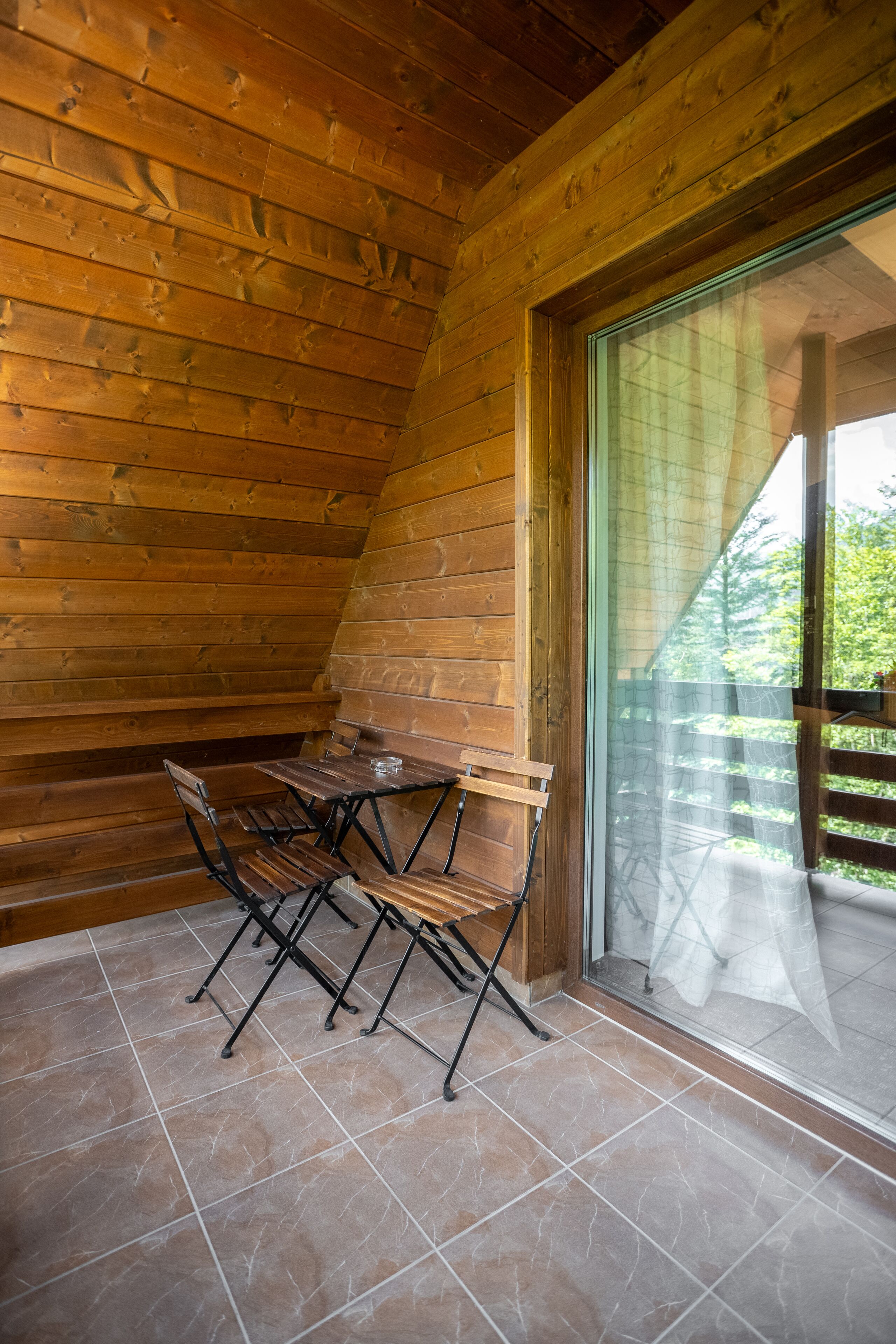 A wooden cabin with a dining table and chairs, a large sliding glass door, and a view of greenery outside.