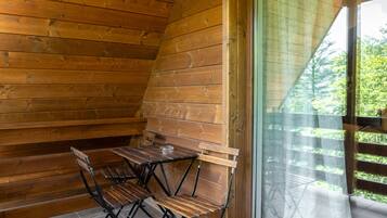 Una cabaña de madera con una mesa y sillas de comedor, un amplio ventanal corredizo y vistas a la vegetación.