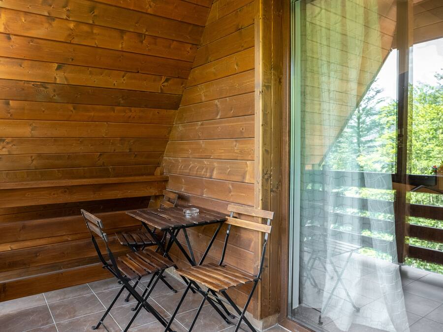 Una cabaña de madera con una mesa y sillas de comedor, un amplio ventanal corredizo y vistas a la vegetación.