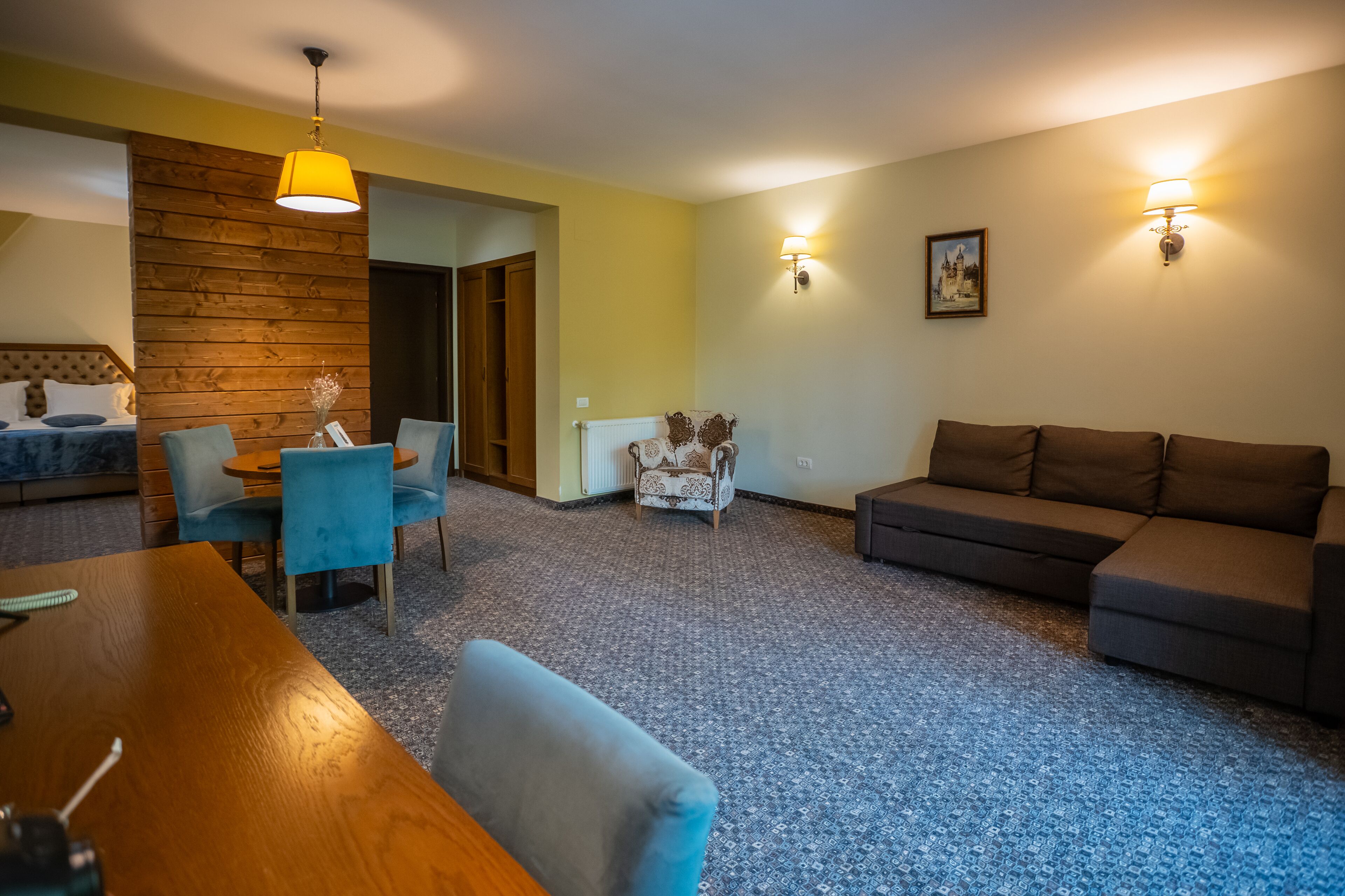 Una habitación con un muro decorativo de madera, una mesa de comedor con sillas, un sofá y dos lámparas fijadas a la pared.