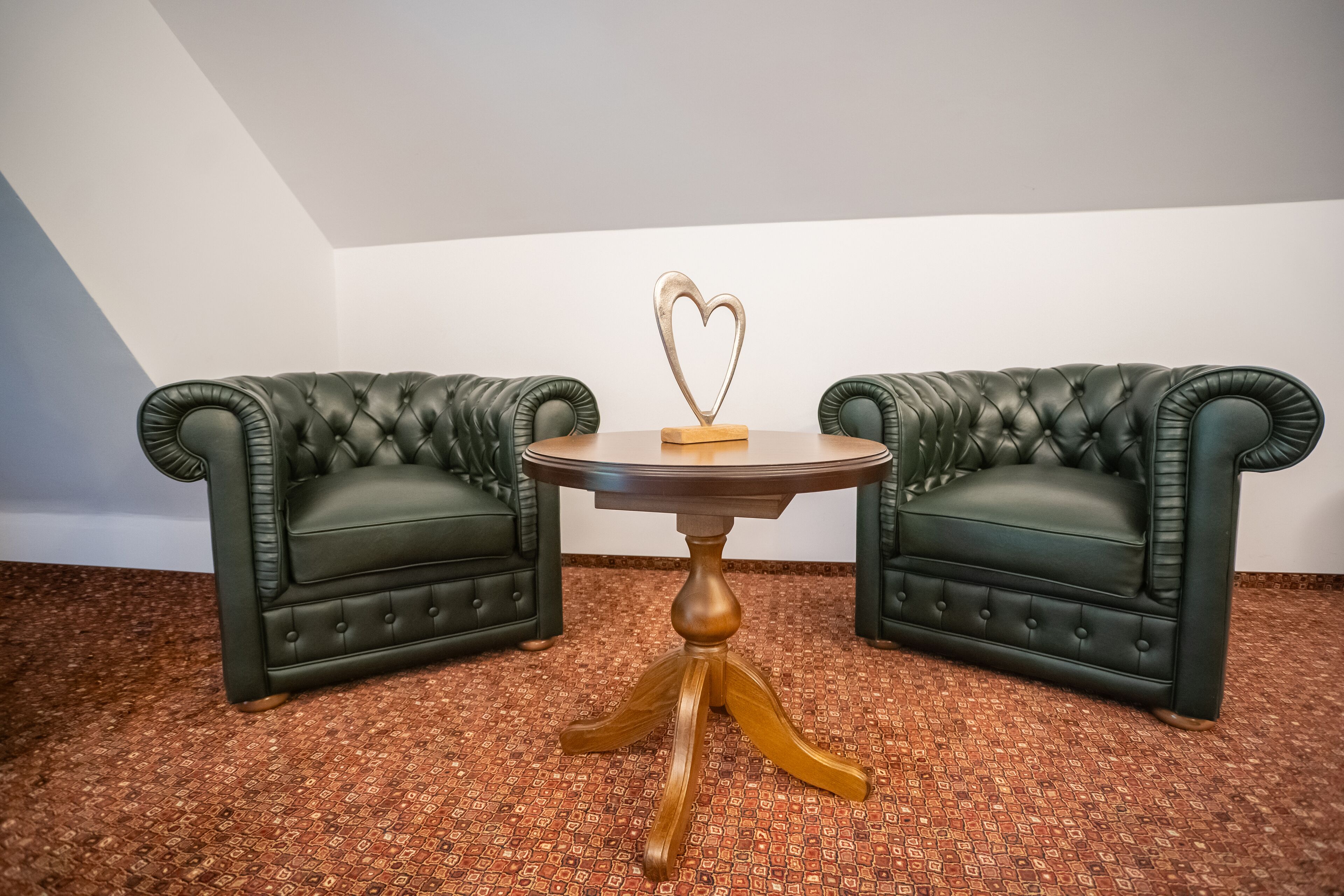 Una habitación con dos sillones de cuero verde y una mesa de madera con un adorno con forma de corazón.