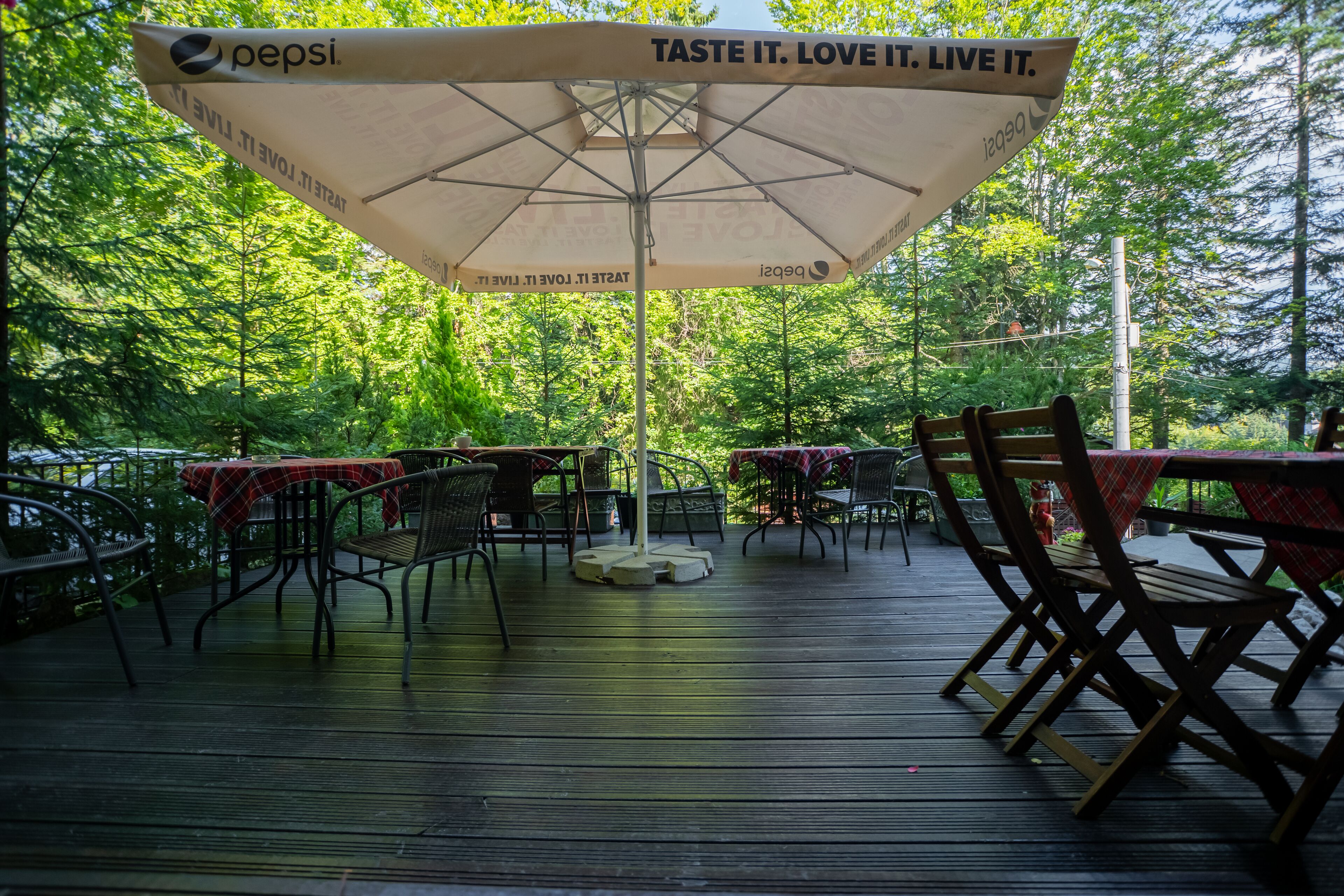 An outdoor patio area with tables and chairs, covered by a large umbrella with Pepsi branding.