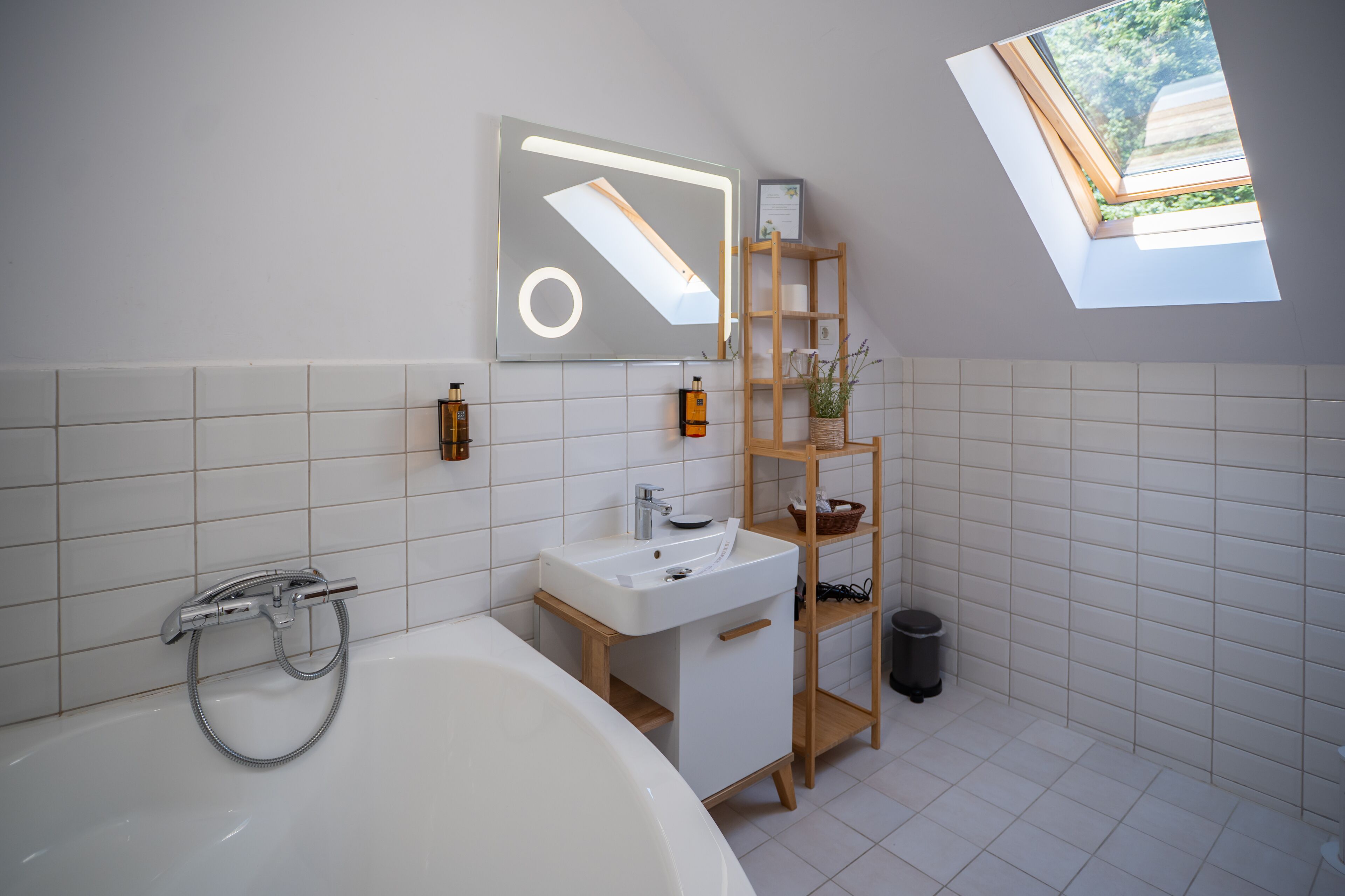 A modern bathroom with a freestanding bathtub, a white sink, a wooden vanity, and a skylight.