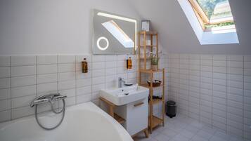 Un baño moderno con una bañera independiente, un lavabo blanco, un tocador de madera y un tragaluz.