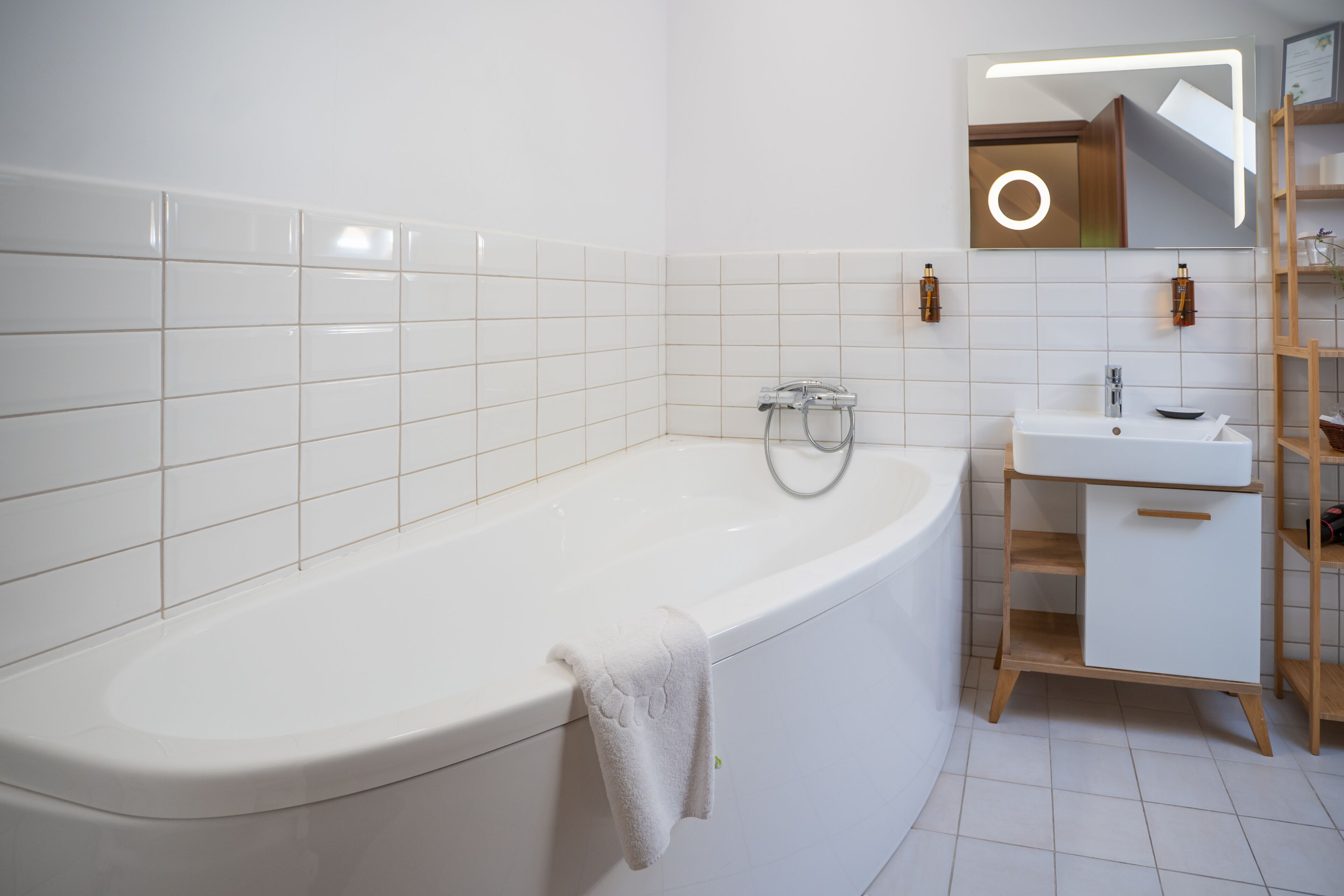 A modern bathroom with a freestanding bathtub, a white sink, and a mirror with a circular light.