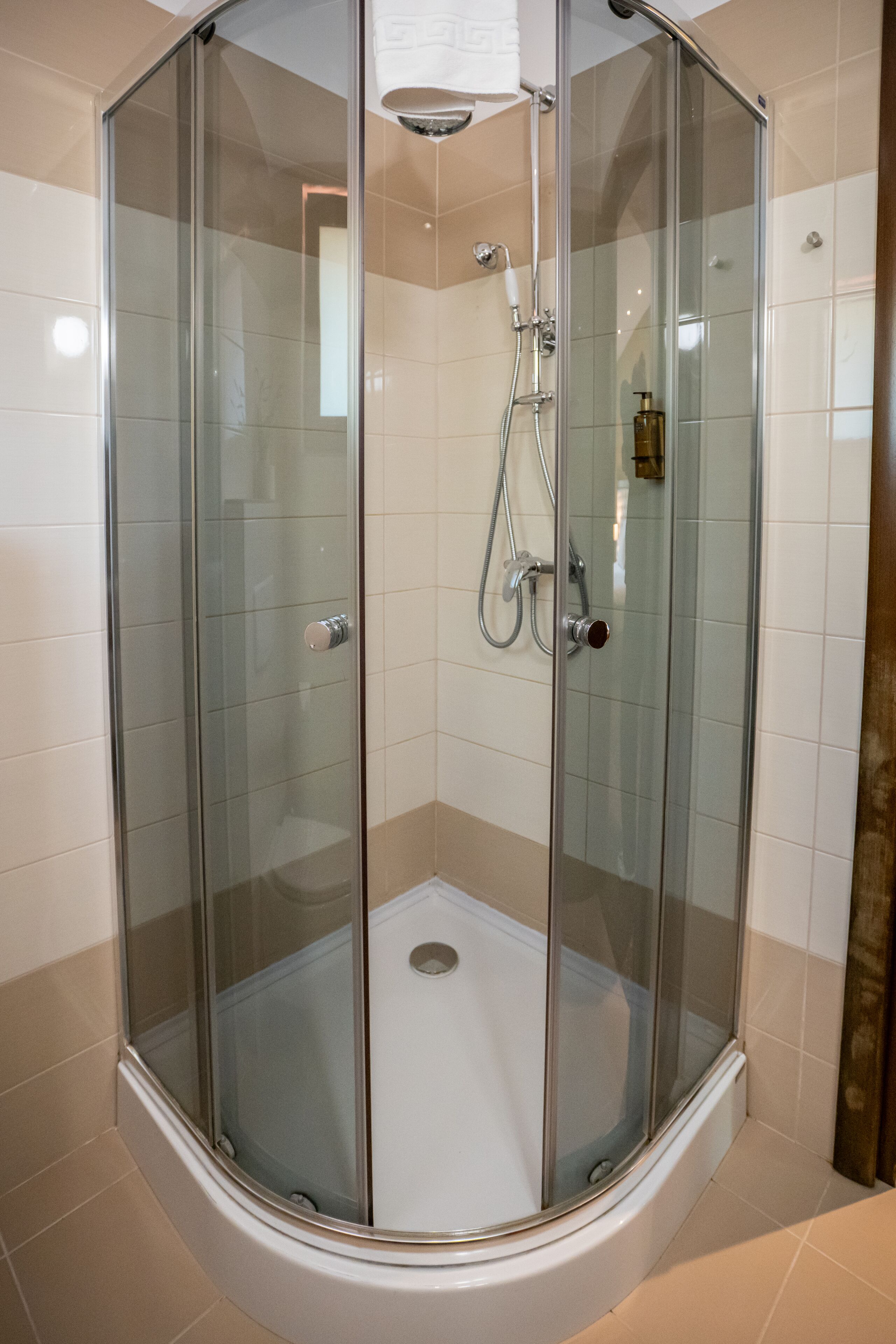 A glass-enclosed shower stall with a white floor, a handheld showerhead, and a wall-mounted faucet.