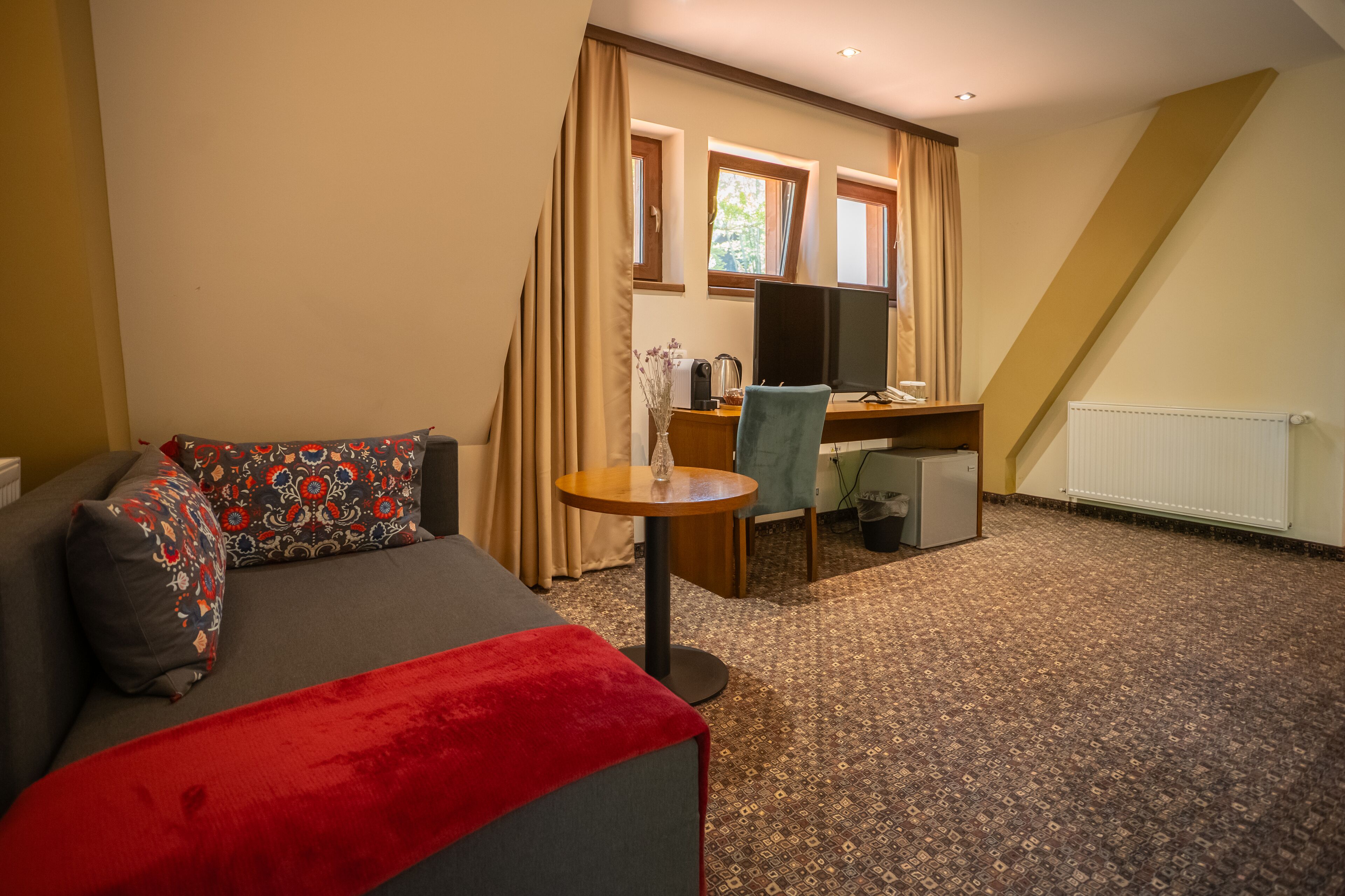 A furnished room with a sofa, a small table, a desk with a computer, and a radiator.