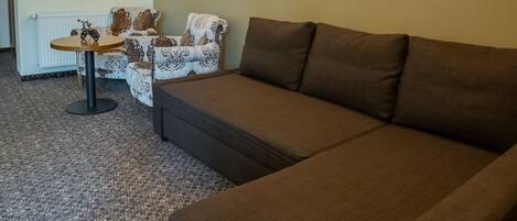 A living room with a brown sofa, patterned armchairs, a small table, and wall-mounted lighting.