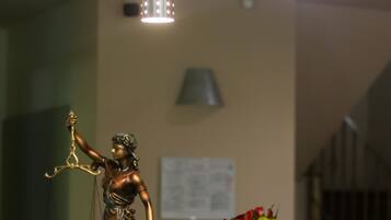 Una estatua de la Justicia sobre una mesa con un jarrón de flores y una lámpara al fondo.