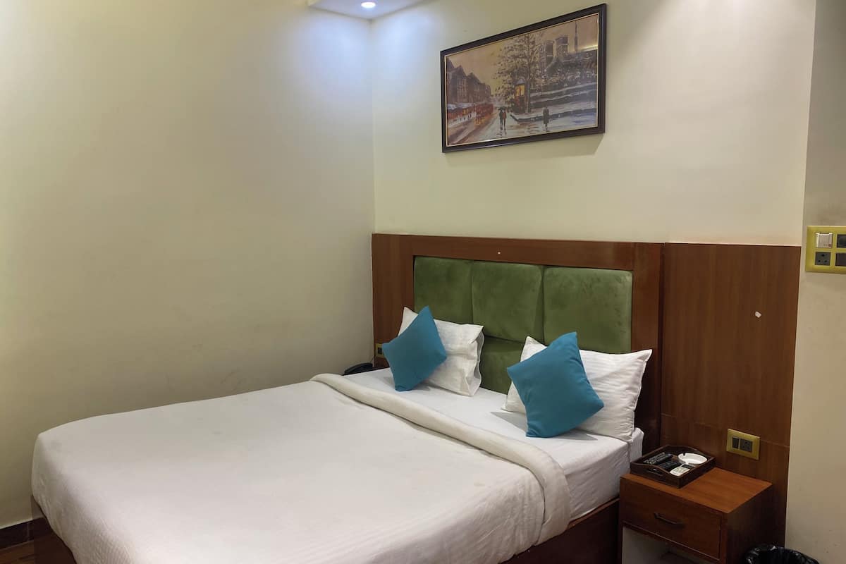 Habitación de hotel con cama, mesita de noche, un cuadro colgado en la pared y cabecero de madera.