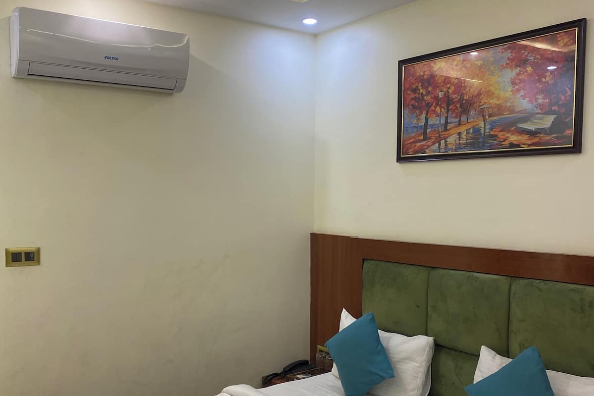 Una habitación de hotel con una cama, un ventilador de techo, un equipo de aire acondicionado y un cuadro en la pared.