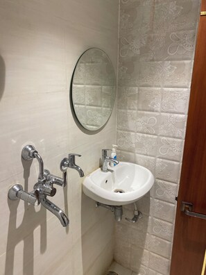 A bathroom with a white sink, a mirror, and a shower with chrome fixtures. - Ramesh Palace (Prayagraj)