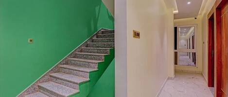 Una escalera con un lado adosado a una pared verde y el otro a una pared blanca.