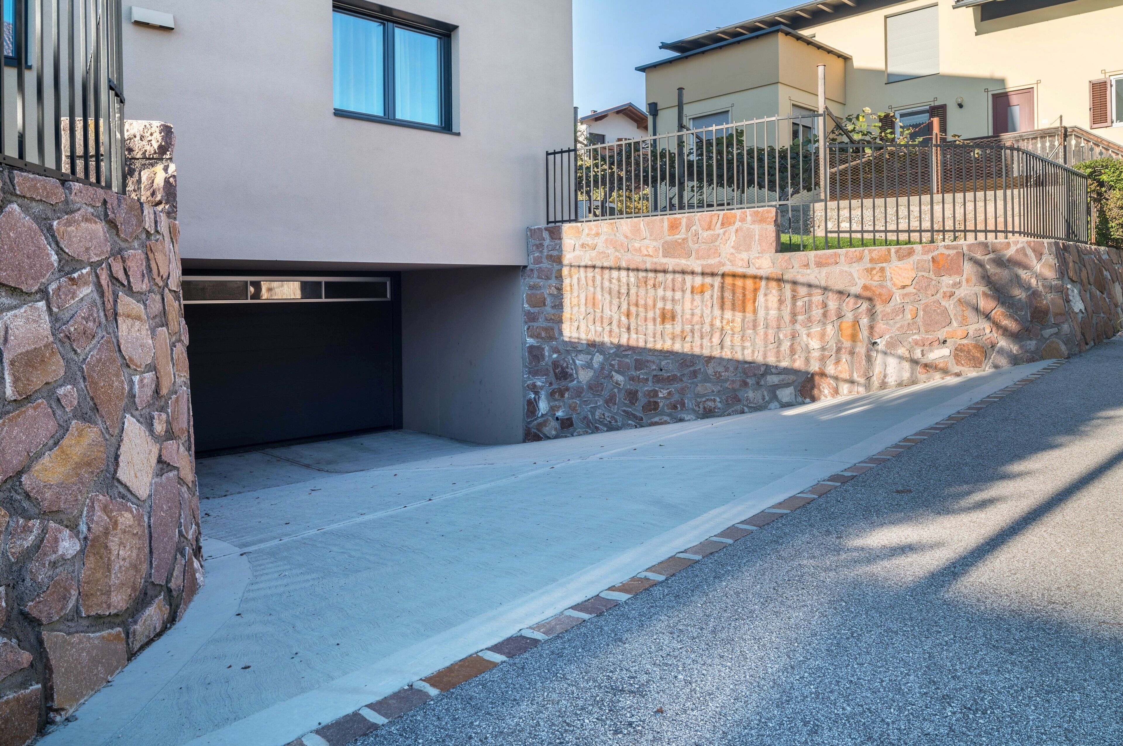 A modern building with a stone wall, a metal fence, and a paved driveway.