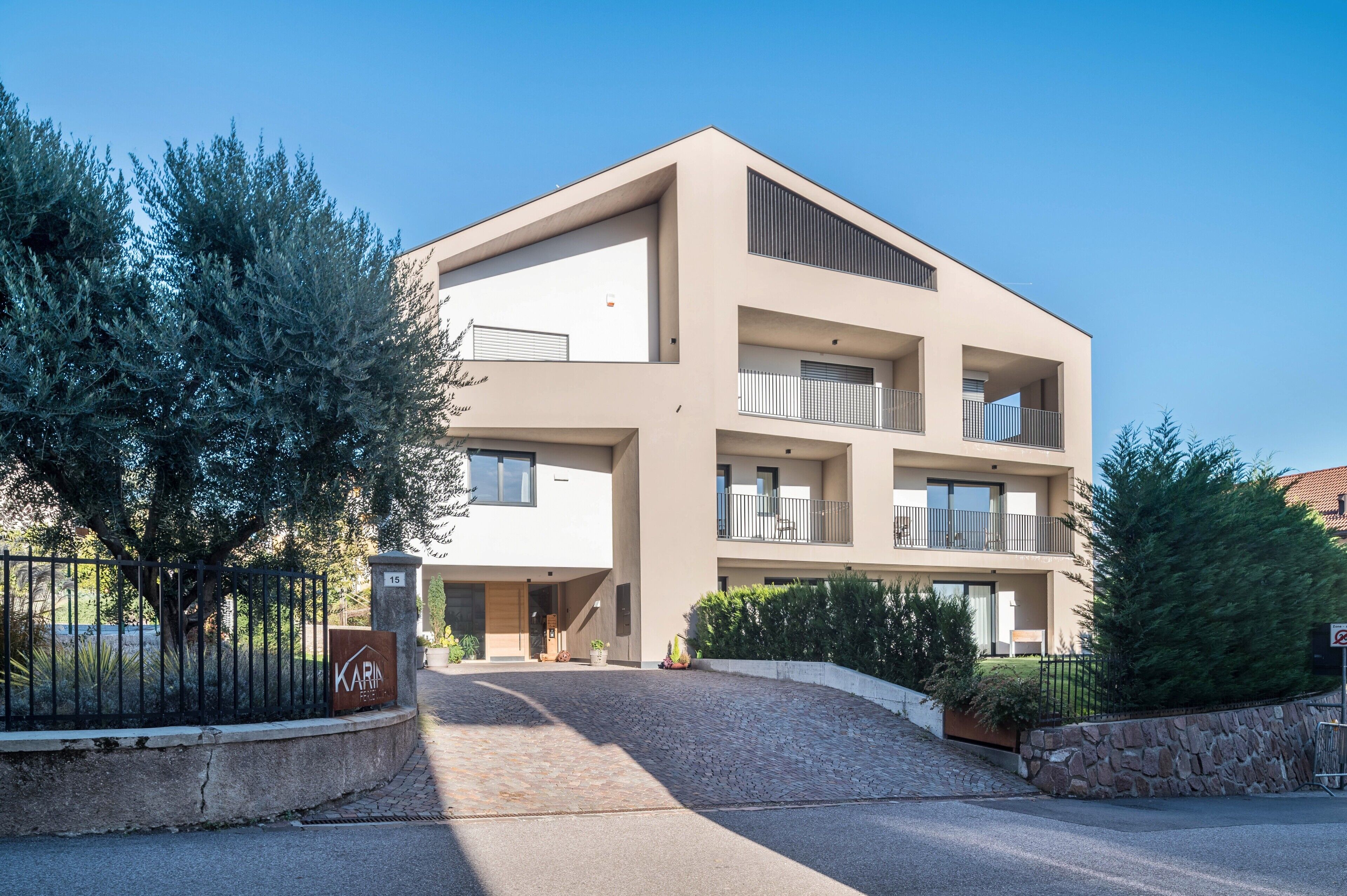 Un immeuble moderne à plusieurs étages, doté d’un toit plat, de balcons et d’un espace d’entrée pavé.