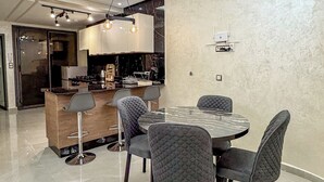 Une cuisine moderne dotée d’un îlot central, de luminaires suspendus et d’un coin repas avec une table ronde et des chaises rembourrées.