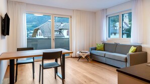 A modern living room with a dining table, sofa, and large windows offering a view of buildings and hills. - Holiday Apartment "Karin - Cabernet" with Shared Terrace and Wi-Fi (Termeno)