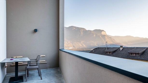 A balcony with a table and chairs, a view of mountains, and a building with a sloped roof. - Holiday Apartment "Karin - Cabernet" with Shared Terrace and Wi-Fi (Termeno)