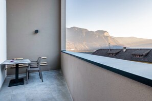 Un balcon avec une table et des chaises, une vue sur les montagnes et un bâtiment doté d’un toit en pente.