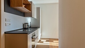 Uma cozinha moderna com bancada preta, prateleiras de madeira e painel de fundo claro.