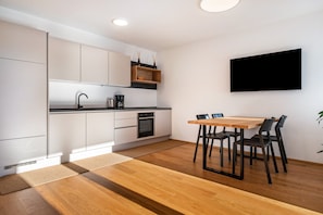 Una cocina moderna con armarios blancos, una mesa de comedor de madera y un televisor de pantalla plana montado en la pared.