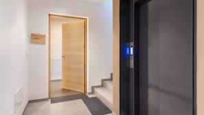 Un couloir avec une porte en bois, une porte d’ascenseur noire et un petit panneau sur le mur.