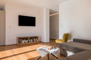 A modern living room with a flat-screen TV, a bookshelf, a small table with a box, and a sofa. - Apartment 'Karin - Golden' with Shared Terrace and Wi-Fi (Termeno)