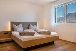 Une chambre moderne avec un lit en bois, du linge de lit blanc et une fenêtre donnant sur les montagnes.