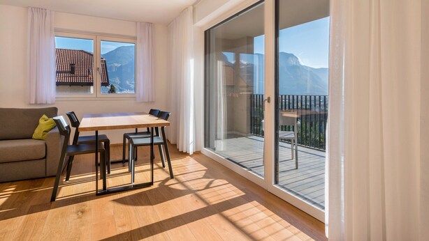 A room with a dining table, chairs, a sofa, and a balcony with a view of mountains. - Apartment "Karin - Golden" with Shared Terrace and Wi-Fi (Termeno)