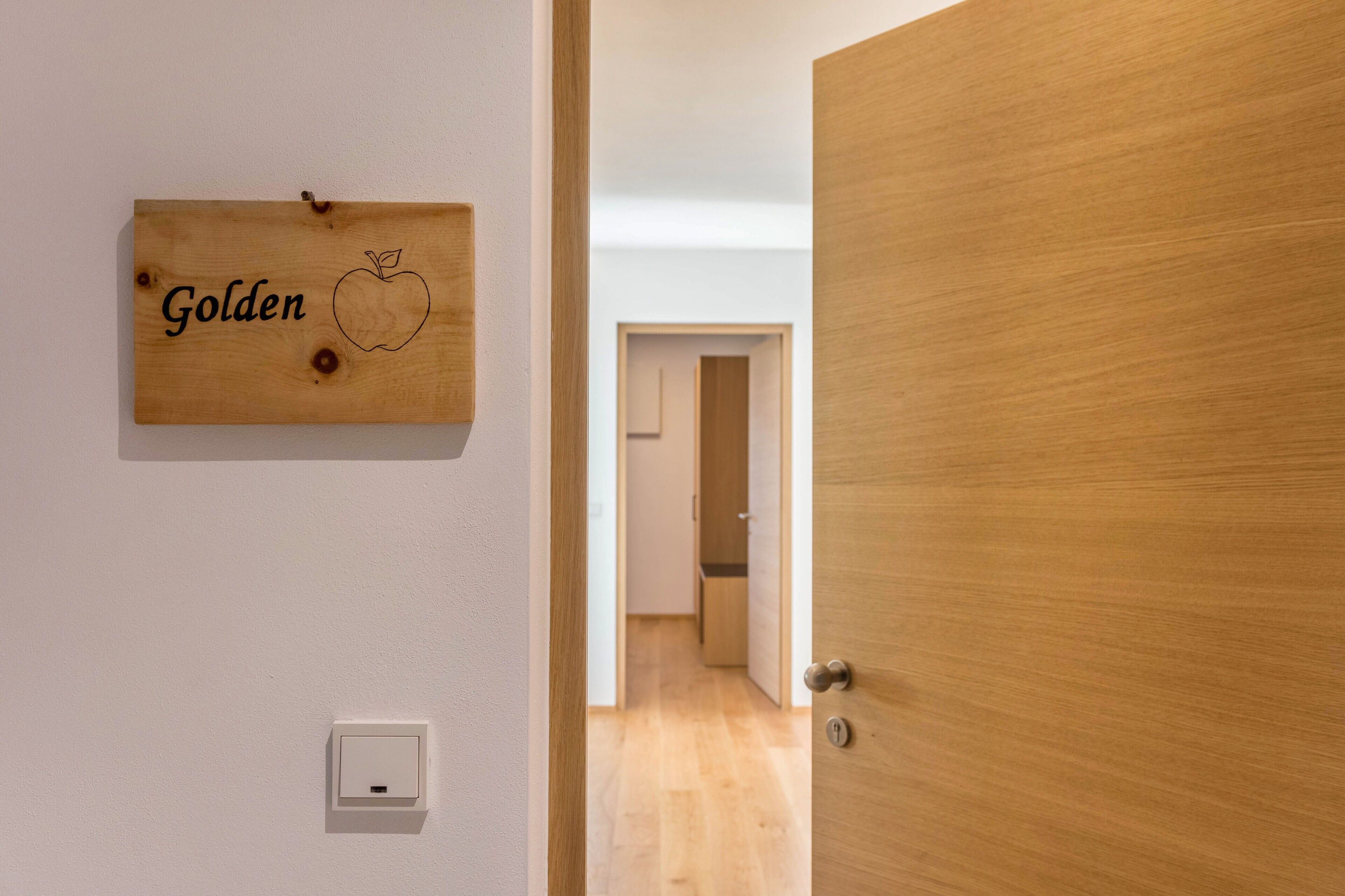 A wooden door with a handle, a wall-mounted light switch, and a wooden plaque with the word 'Golden' and an apple drawing.