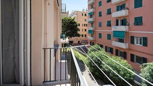 A multi-story residential building with balconies, a clear sky, and a tree in the courtyard.