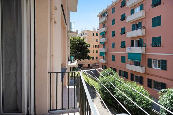 A multi-story residential building with balconies, a clear sky, and a tree in the courtyard.