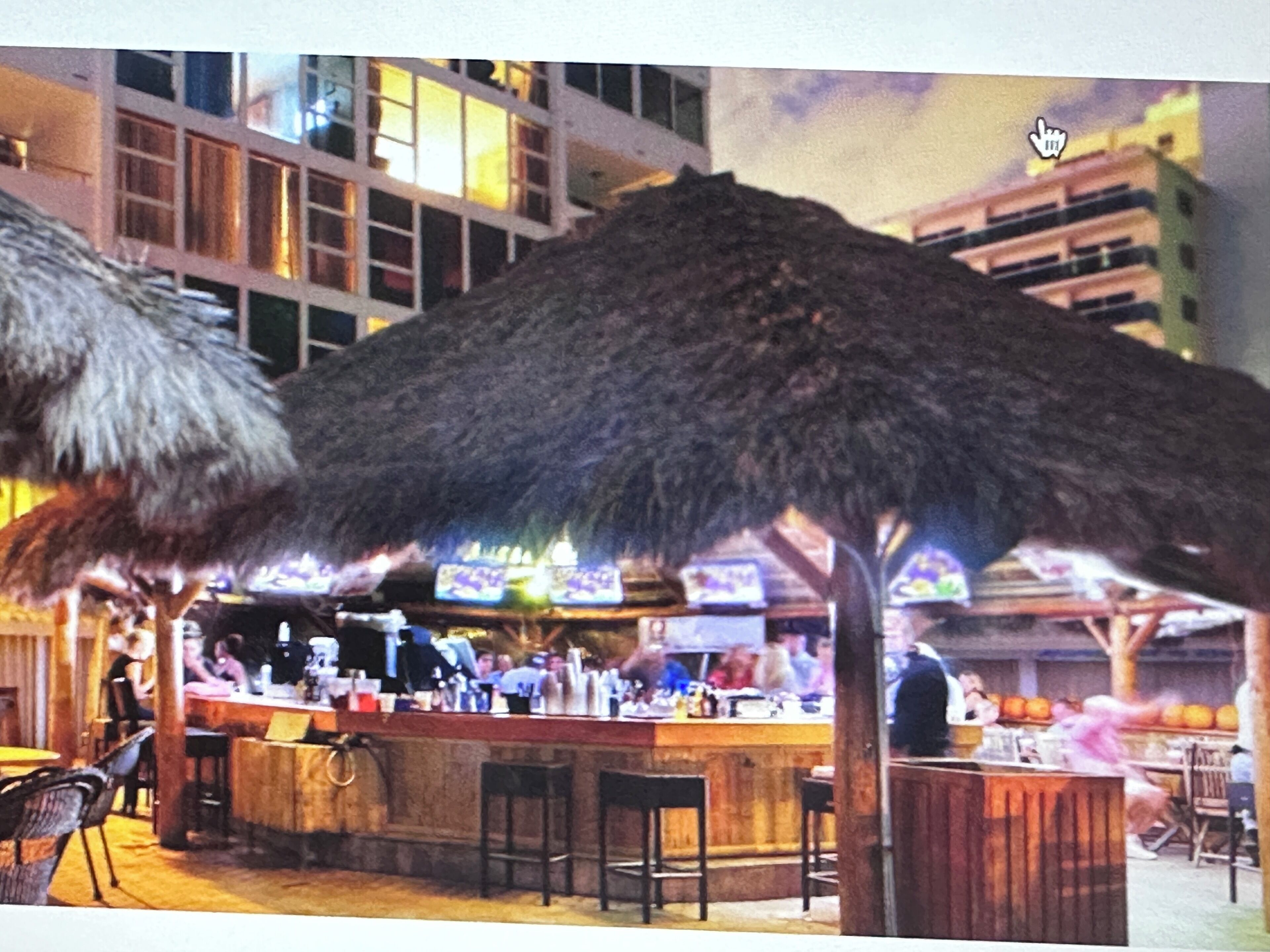 A bar area with a thatched roof, wooden bar counter, and several stools.