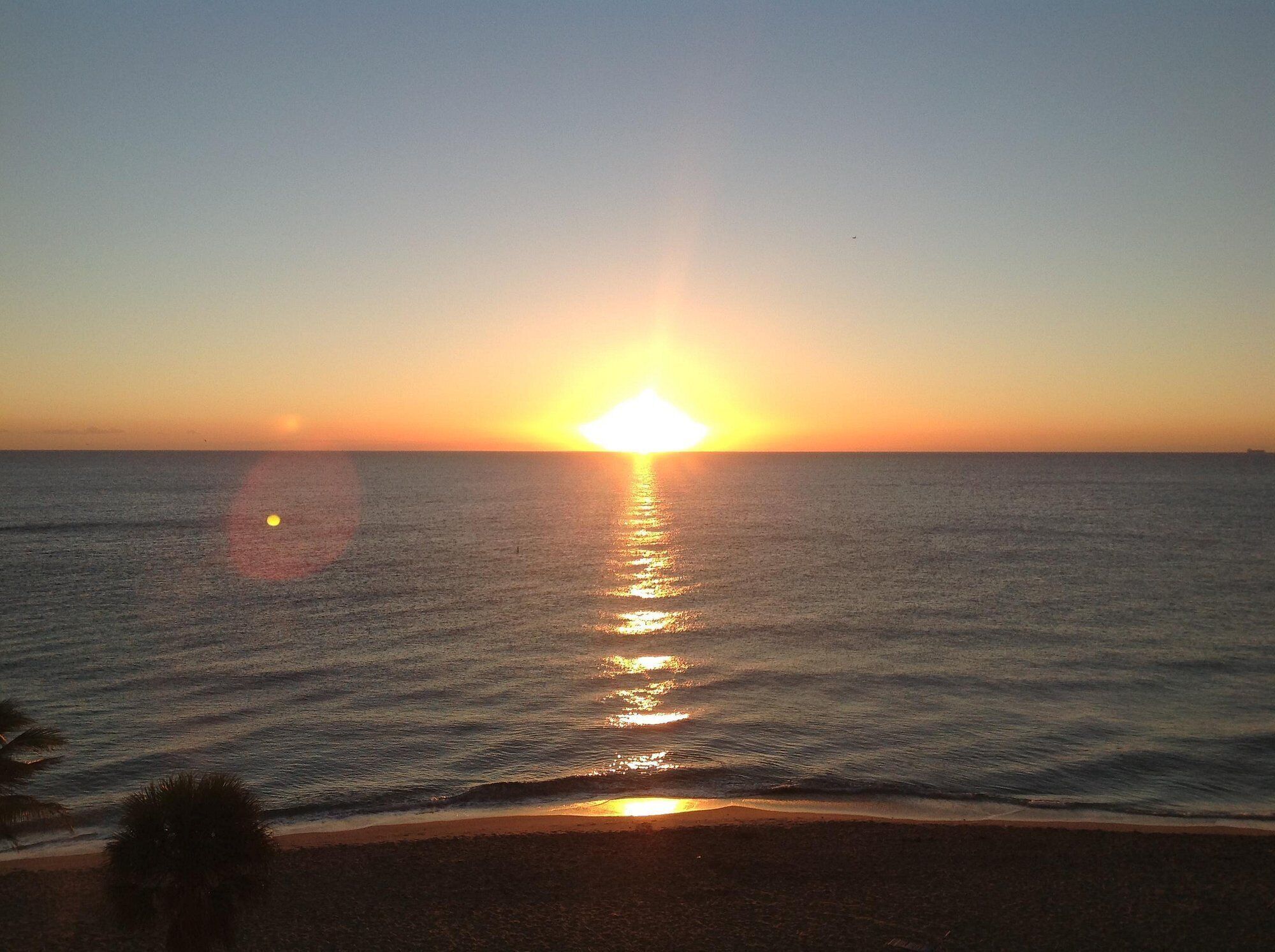 Un coucher de soleil sur l’océan, avec une plage au premier plan.