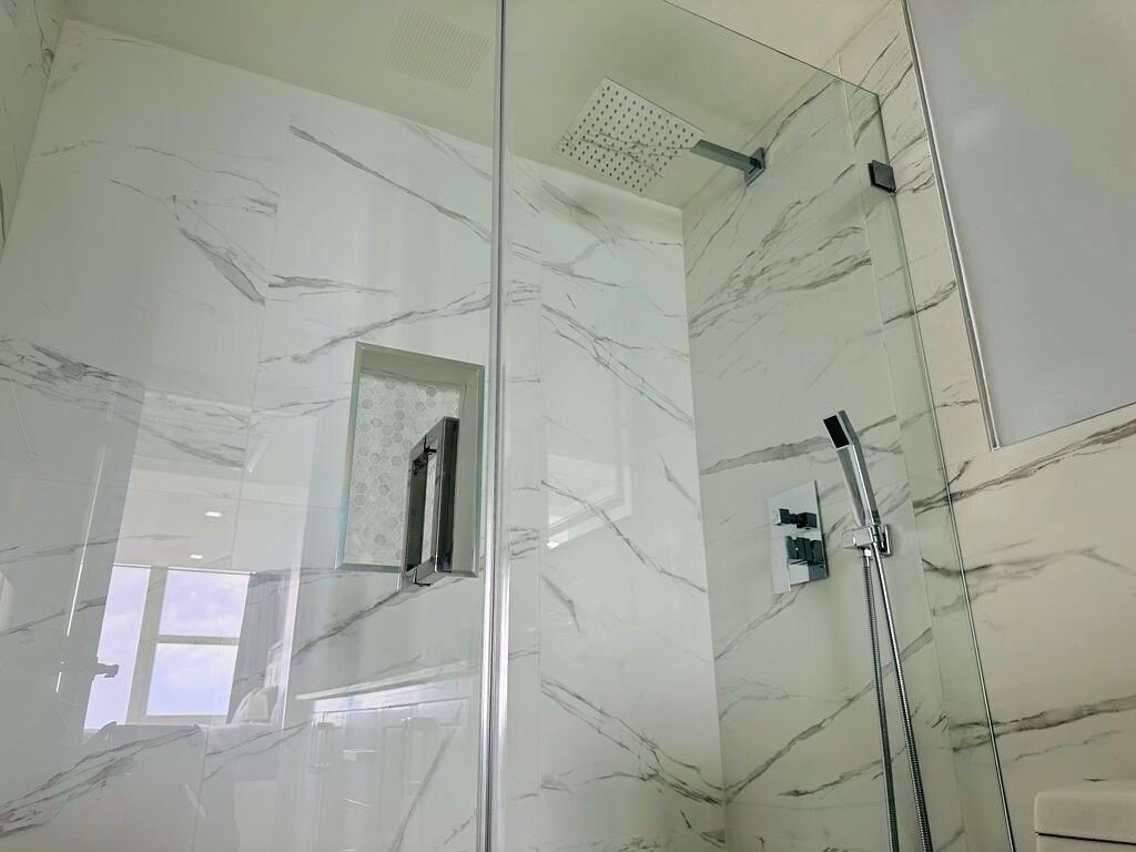 A modern bathroom with marble walls, a glass shower enclosure, and a visible window.