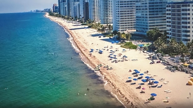 A coastal cityscape with a beach lined with high-rise hotels, clear blue waters, and sunny skies.