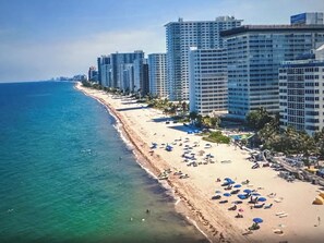 Un paisaje urbano costero con una playa bordeada por altos hoteles, aguas azules cristalinas y cielos soleados.