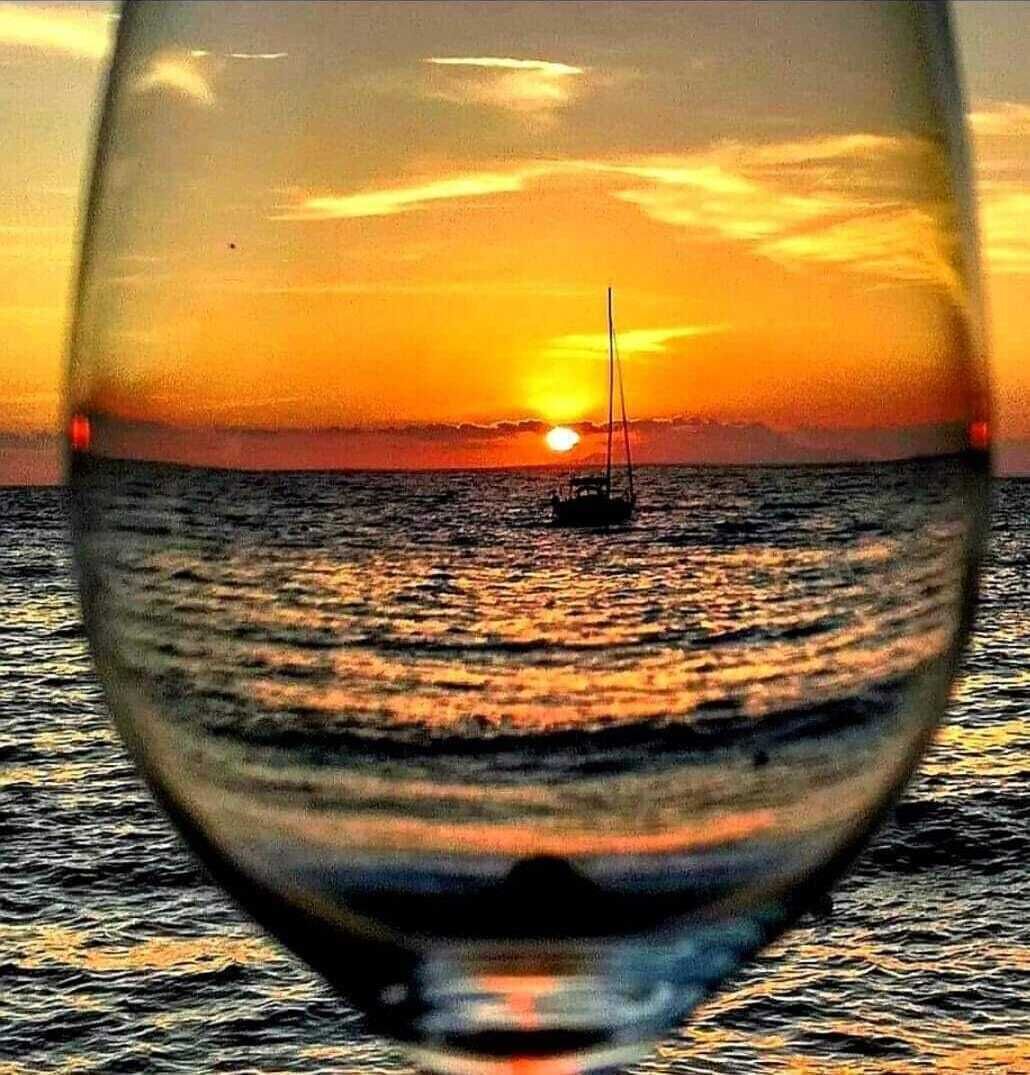 Ein Glas mit Sonnenuntergang und einem Segelboot auf dem Wasser.