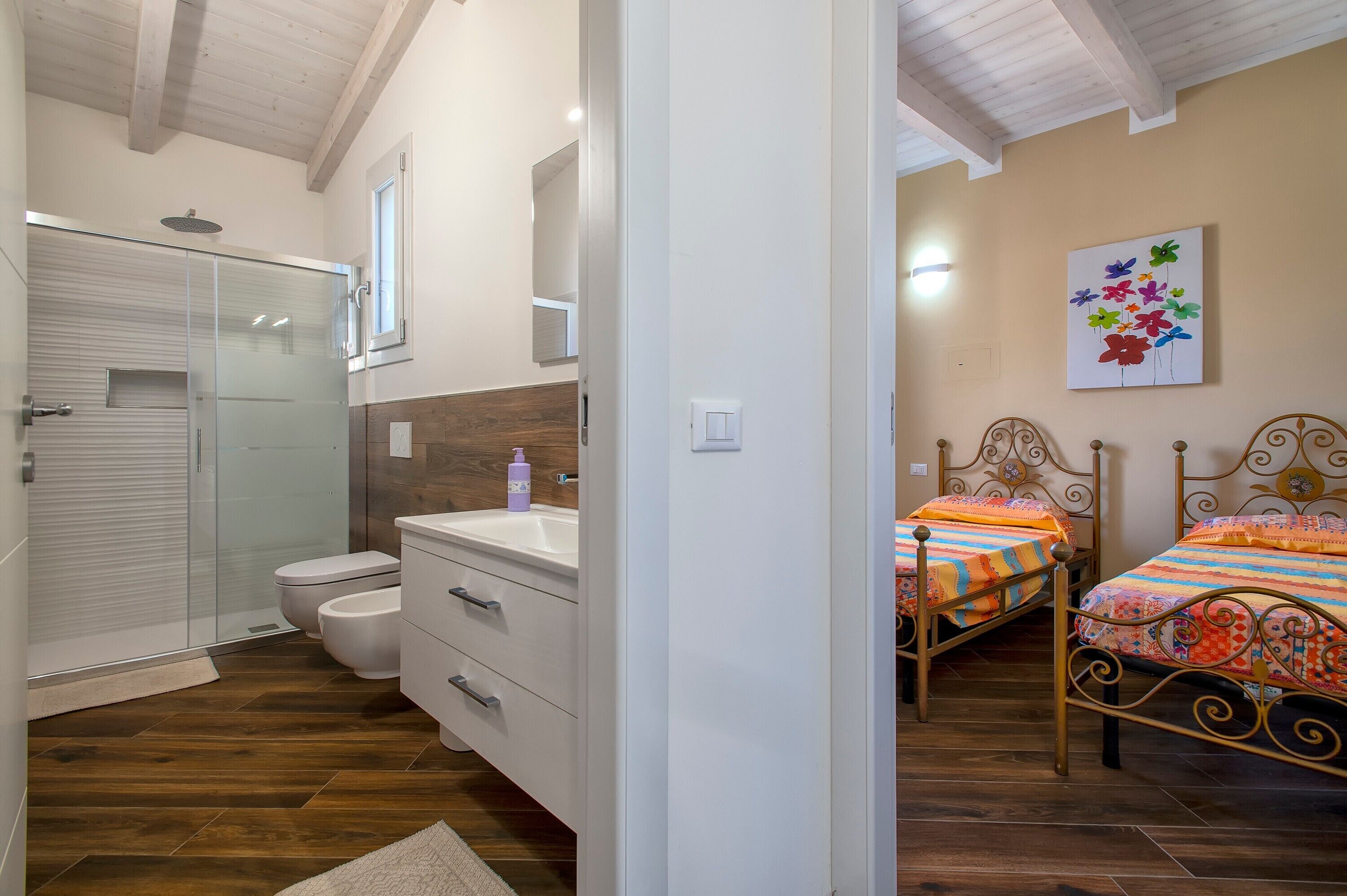 A bedroom with two beds, a bathroom with a shower, and a wooden floor.