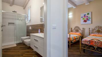 A bedroom with two beds, a bathroom with a shower, and a wooden floor.